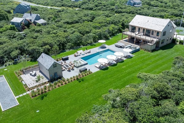 Modern coastal home with pool, hot tub, and manicured lawn overlooking beach and neighboring houses