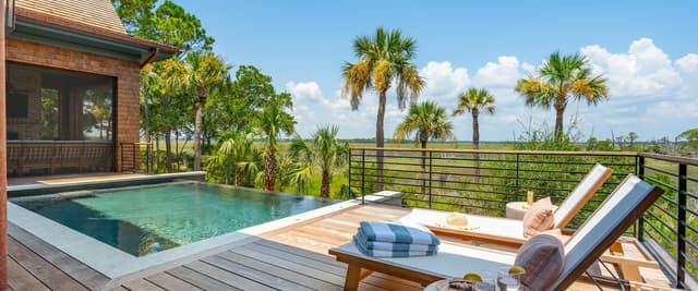 Luxury poolside patio with infinity pool, palm trees, cabana daybed, umbrellas, and tropical landscaping
